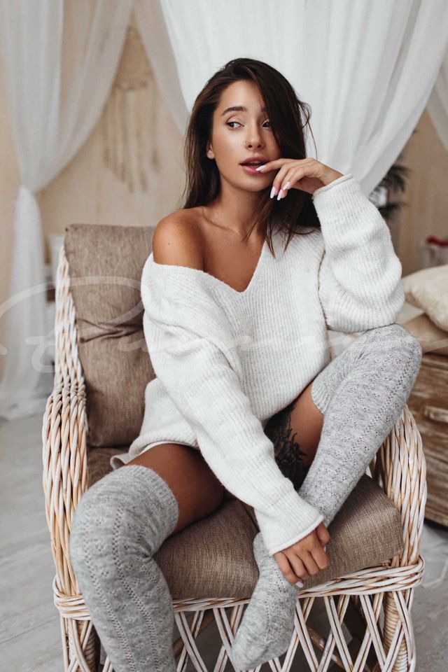 Mona sitting on a chair wearing a white sweater and gray leg stockings